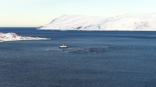 Snowy mountain landscape surround salmon farm with pens and barge. Aerial