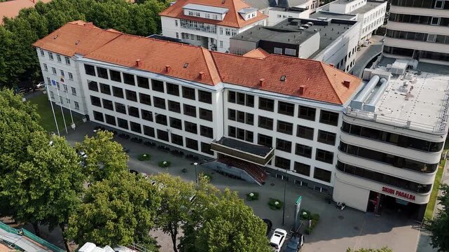 Emergency department facade of Respublikinė Klaipėdos ligoninė is seen from above with an ambulance parked by the entrance and pedestrians nearby.