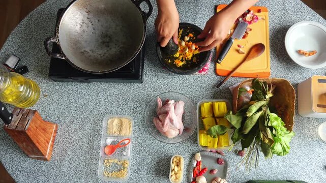Overhead view of chef vigorously grinding yellow and red spices inside stone mortar using pestle