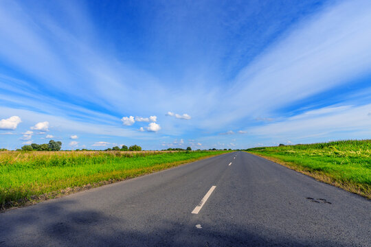 Asphalt road stretches toward distant horizon under vast blue sky