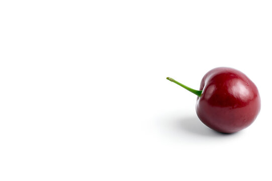 A single ripe red cherry with glossy skin and long curved green stem, isolated on pure