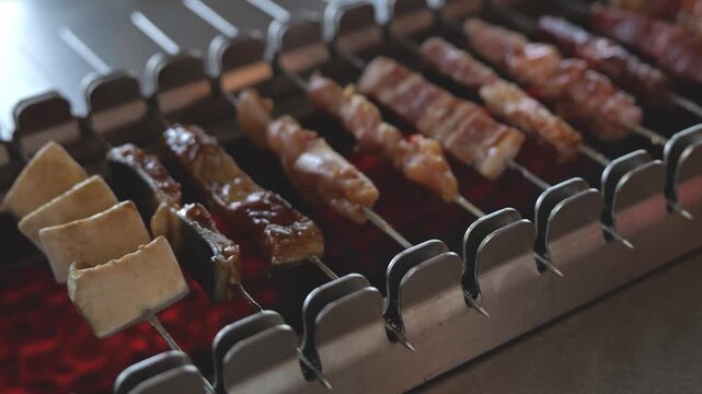 Close-up of assorted meat skewers rotating automatically over a hot BBQ grill, capturing sizzling meat, rising smoke, and appetizing grilled textures.