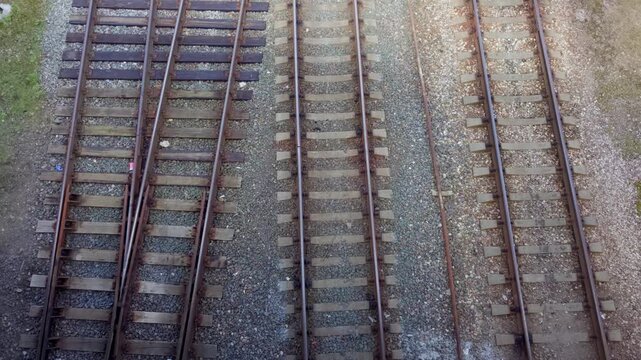 Direct top down shot looking at multiple parallel railway tracks and wooden ties laid on gravel ballast with rail switch in Daugavpils Latvia during daytime.
