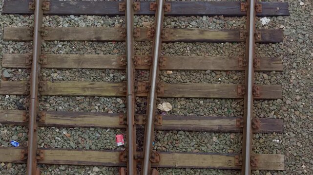 High angle overhead shot looking directly down at railroad switch mechanism on wooden sleepers surrounded by stone gravel ballast in Latvia, presenting industrial texture.