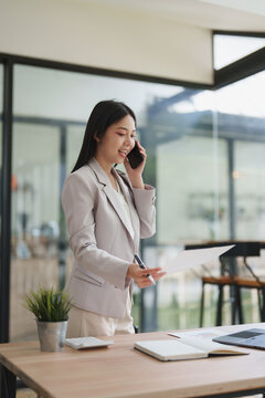 Asian businesswoman talking on smartphone holding document