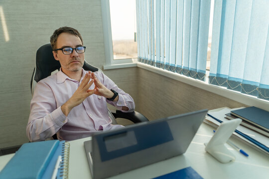Businessman sitting at his office desk with his hands clasped in front of him, looking thoughtful and serious. Business meeting, waiting, or considering important decisions.