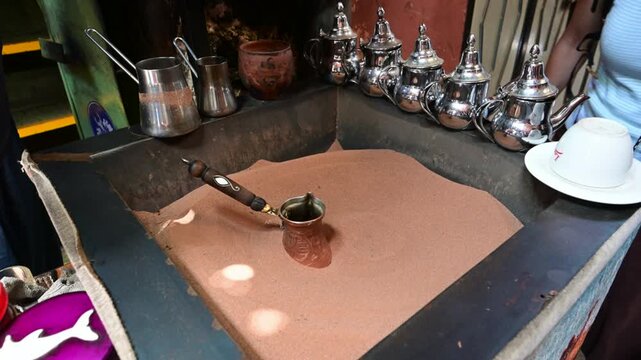 Marrakech, morocco. August 8, 2026. Skilled vendor brewing traditional moroccan coffee in a cezve on hot sand. The authentic process unfolding in a bustling marrakech souk