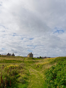 The grassy footpath behind the dunes and down to the Beach at St Combs with the Village seen on the skyline above the sloping ground.