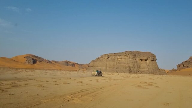Fast-moving car crossing the vast, dry Sahara Desert near Djanet in southern Algeria, surrounded by dramatic rock formations beneath a clear blue sky, capturing the thrill of adventure tourism