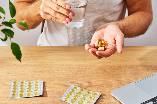 Man taking dietary supplements and vitamins with glass of water at workplace desk