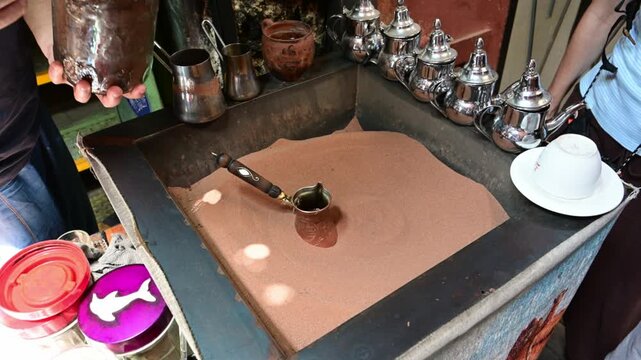 Marrakech, morocco. August 8, 2026. Man's hands preparing authentic hot coffee using a traditional cezve in hot sand. Famous street food beverage in a souk in marrakech, morocco