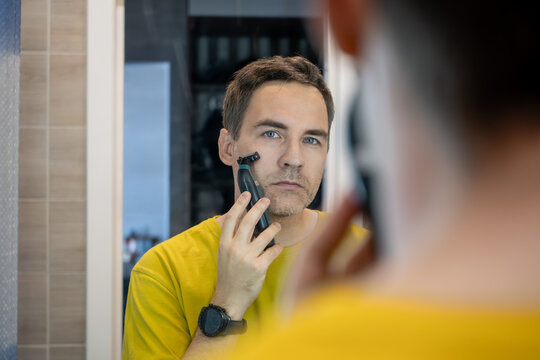 Man shaving with electric razor in front of mirror, morning grooming routine.