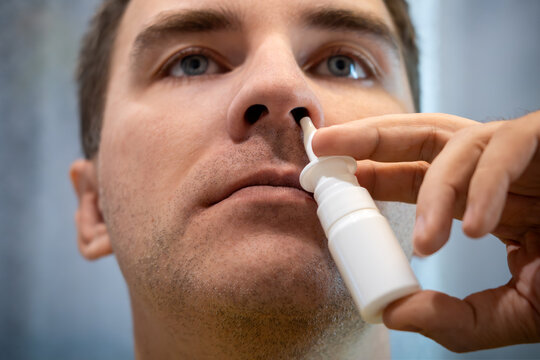 Man using a nasal spray to treat a stuffy nose and congestion, looking at the camera. Allergy relief, sinus treatment, and cold symptoms.