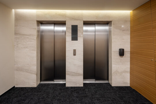 Modern elevator hall interior with stainless steel doors and travertine stone wall