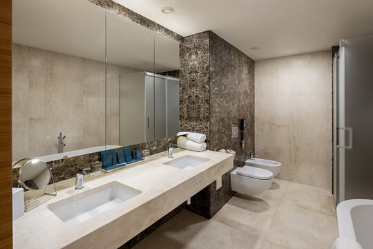 Spacious luxury bathroom with double sink vanity tub bidet and marble wall