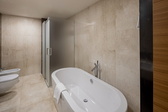 Modern hotel bathroom interior featuring white freestanding bathtub and shower cabin