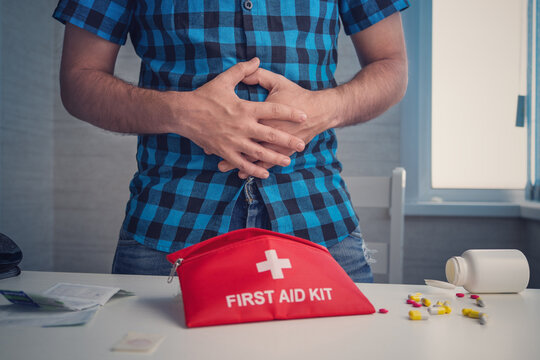Man holding his stomach in pain, standing near a table with a first aid kit. Stomach ache, diarrhea, constipation, and self-treatment concept.
