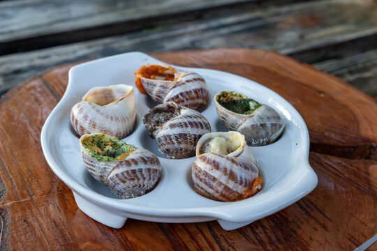 Baked stuffed mollusks are presented with green herb pesto and red spicy tomato sauces inside special white tray on timber background near metal fork outdoors.