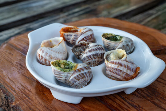 Baked stuffed mollusks are presented with green herb pesto and red spicy tomato sauces inside special white tray on timber background near metal fork outdoors.