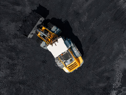 Yellow loader operating on coal pile in mining open pit aerial view