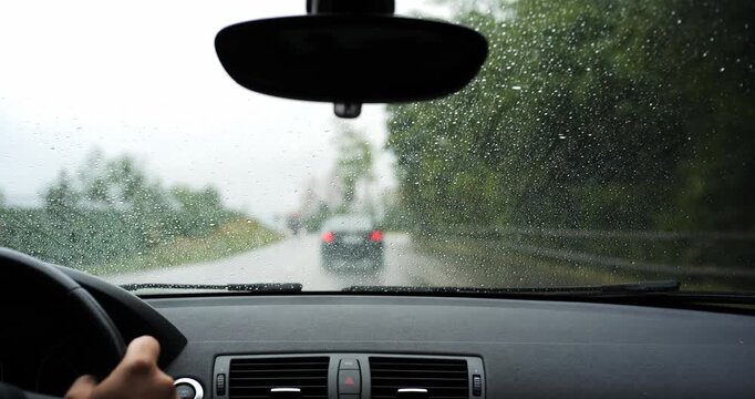 POV shot of driving car on rainy road following a vehicle with oncoming truck traffic. Driver view through wet windshield