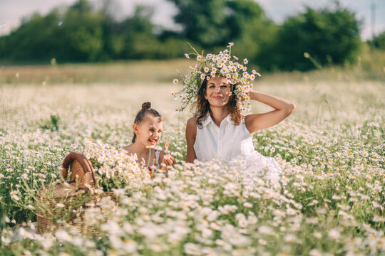 Mother and daughter playing with bubbles in a sunny field of Matricaria chamomilla flowers