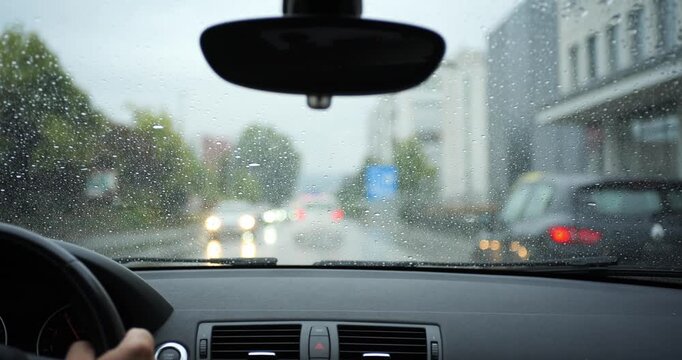 POV shot of driving car on rainy road following traffic in city. Driver view through wet windshield