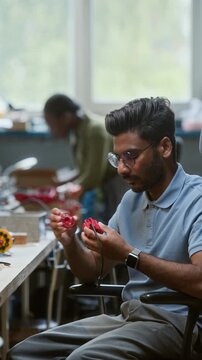 Vertical shot of Indian young adult man with glasses assembling small red electronic component in robotics laboratory. Clip is ideal for tech startups and engineering education promos