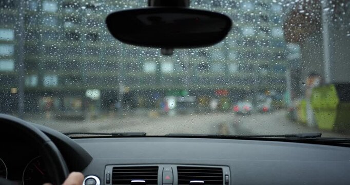 POV car driving on wet city street during rainy weather with raindrops on windshield