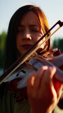 Woman violinist playing outdoors with eyes closed, immersed in emotional music performance at golden hour, sunlight highlighting instrument and serene expression