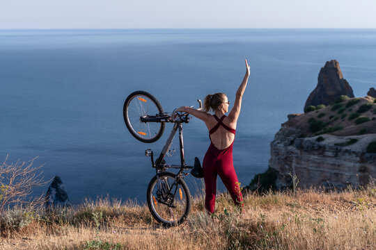 Bicycle travel woman holding mountain bike high above scenic coastal cliffs during a sunny summer vacation outdoors