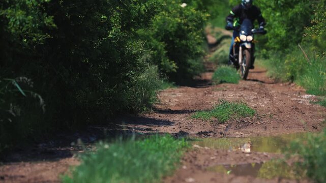 Enduro rider riding motorcycle on dirt trail and splashing through mud puddle outdoor