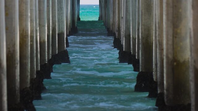 Long lens shot of waves crashing on to the pylons underneath a pier