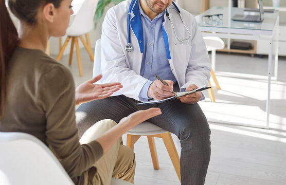 Young woman patient talking to female doctor in office during medical examination. Man physician listening and writing down the patient's complaints in clinic. Healthcare and medicine concept.