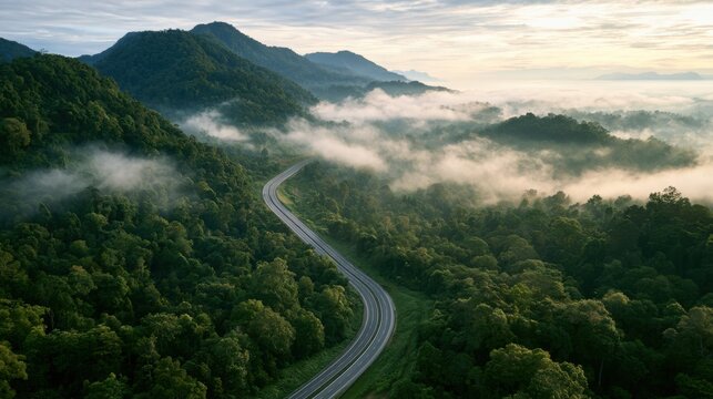 Aerial view of a winding highway cutting through lush tropical forest and mountain landscape under misty skies
