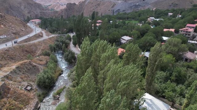 Winding Chalus Road follows a mountain river through poplars and scattered village roofs in a green Iranian highland valley. Ideal for travel, tourism, and nature stock Iran Alborz valleys.