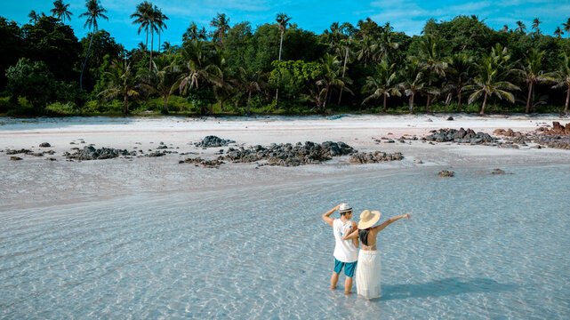 Couple tourist stay happy moment at the edge of the sea beach under shallow of the crystal clear water in summer trip on tropical island island