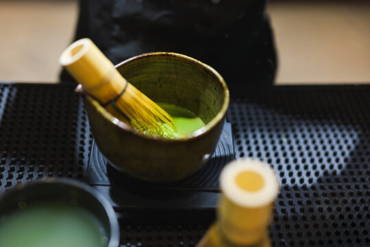 Matcha green tea with traditional bamboo whisk resting inside a ceramic bowl.