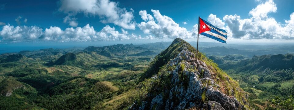 View of Cuba's flag waving from a mountain peak with green hills and blue sky in the background during daytime