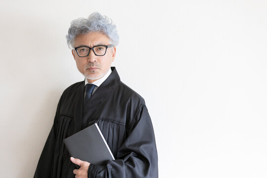 法律書を手にカメラを見つめる法服姿の男性裁判官

