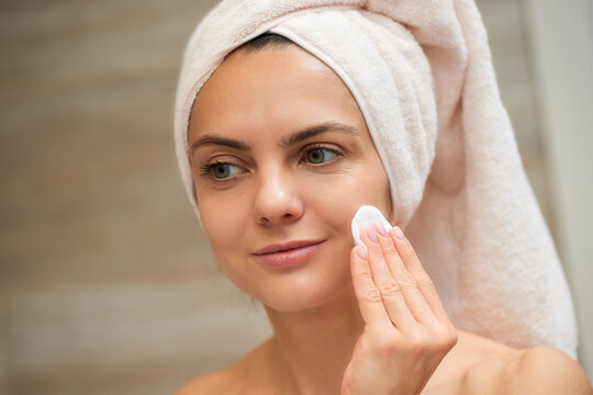 Woman cleansing face with cotton pad in bathroom