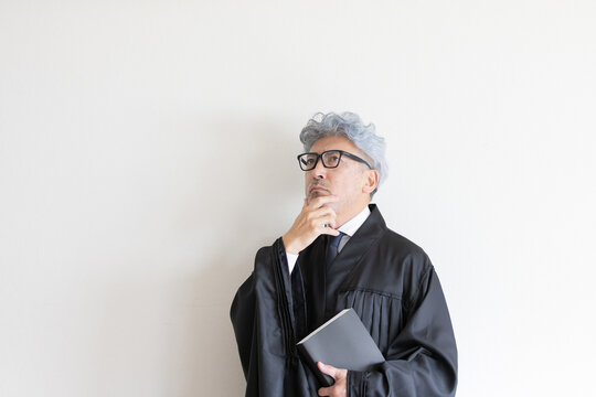 法服姿で本を持ちながら判決について考える男性裁判官
