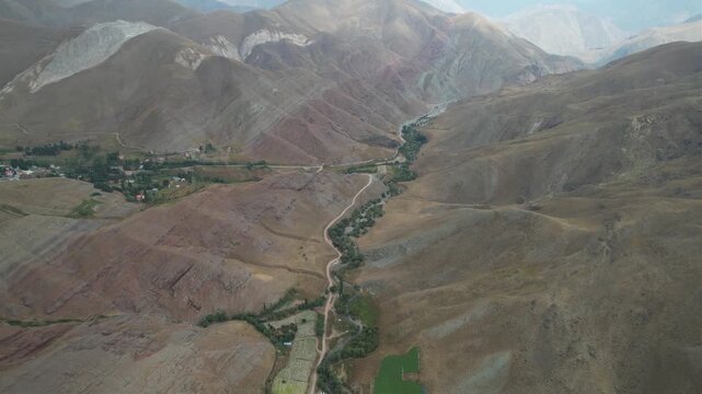 Aerial Chalus Road canyon shows a thin green valley floor cutting through wide brown mountain ridges under a pale sky. Ideal for travel, tourism, and nature stock Iran Alborz mountains.
