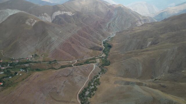 Wide aerial of Chalus Road mountains with a winding green river corridor threading dry slopes across an Iranian highland basin. Ideal for travel, tourism, and nature stock Iran Alborz.