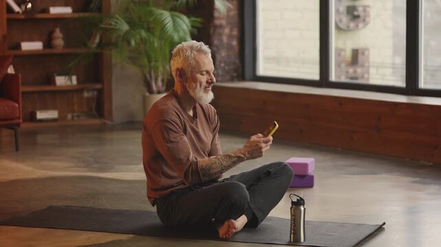 Slim man in his 50s checks fitness tracker app on phone after home workout