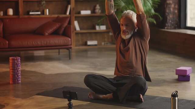 Tattooed middle-aged man records yoga tutorial on phone, fitness blogger