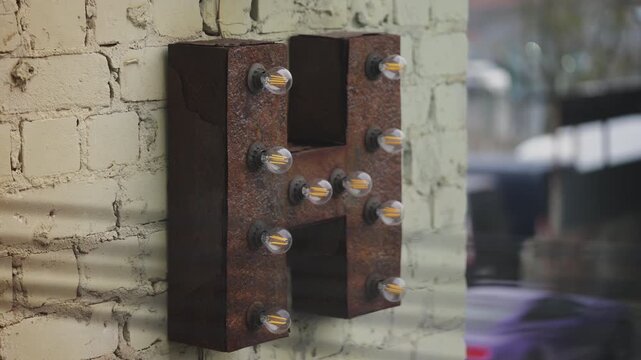 Metal letter H with light bulbs on brick wall, industrial style hotel decor