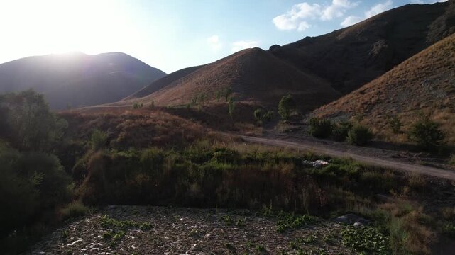 Sun flare over Chalus Road mountains lights a rocky track and dry slopes, backlight across an Iranian highland dirt corridor. Ideal for travel, tourism, and nature stock Iran Alborz valleys.