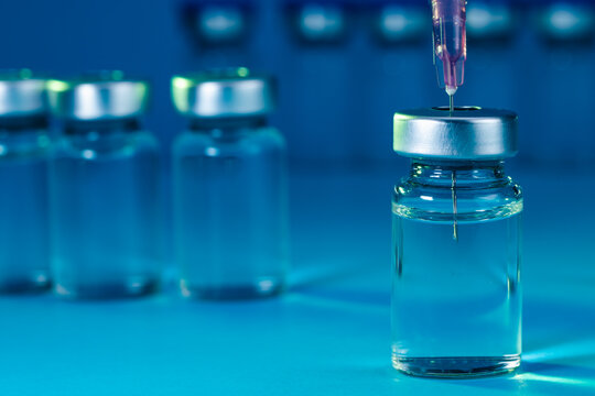 medical syringe with needle next to vaccine medicine glass vials on blue background as a conceptual backdrop for pharmaceutical research healthcare immunization biotechnology and clinical science