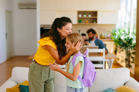 Mother affectionately kissing her daughter goodbye before the girl leaves home for school